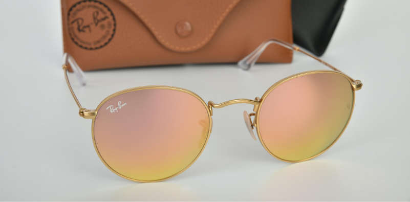 A classic pair of round Ray-Ban sunglasses on the table, in front of a Ray-Ban glasses case.