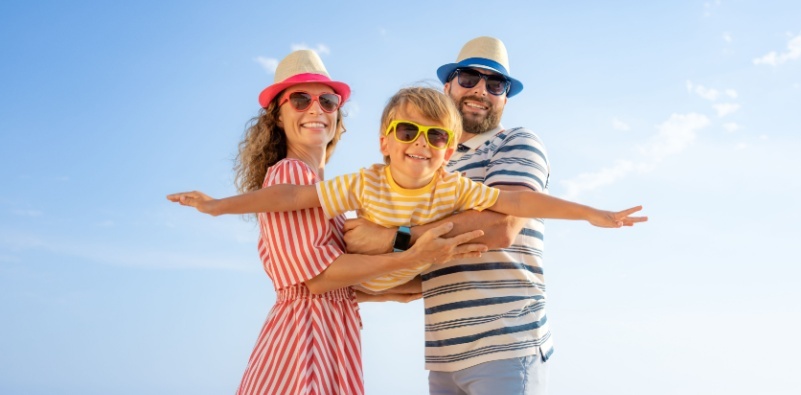 Two adults holding their sun in an aeroplane pose, all wearing sunglasses.