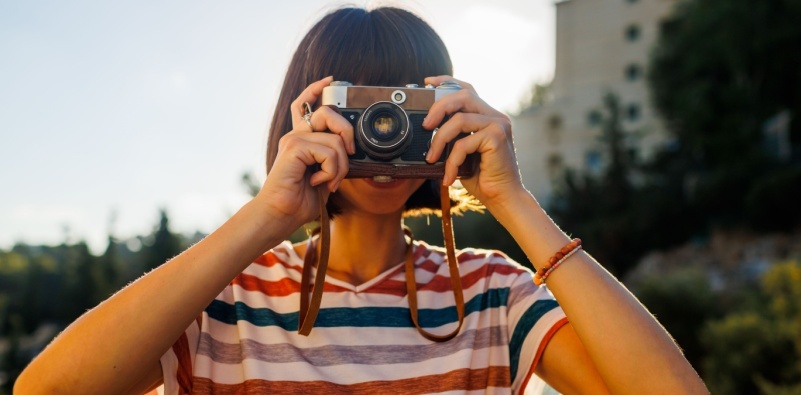 A young woman taking a photo using a vintage-style camera.