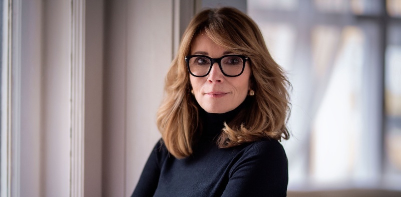 A woman in her late 50’s with blonde hair wearing a pair of black glasses.