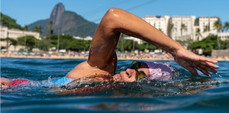 A woman swimming in open water wearing swimming goggles and a pink swimming cap