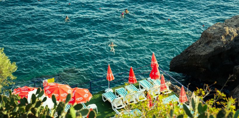 The open sea with people swimming, parasols and sun loungers on the side