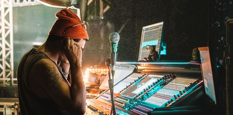 A DJ with his hands to his ears beside his DJ deck