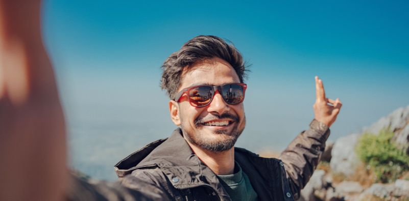 A man taking a picture of himself wearing sunglasses at the top of a mountain.