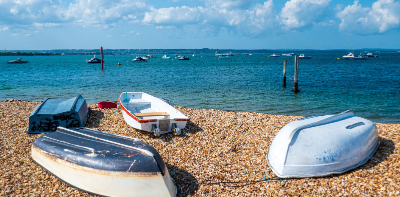 A pebble beach on a sunny day with 4 upturned boats on the beach
