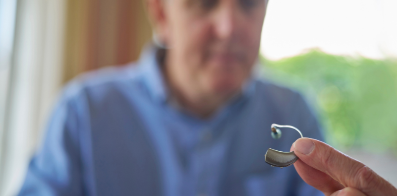 A close-up image of a man holding his hearing aid.