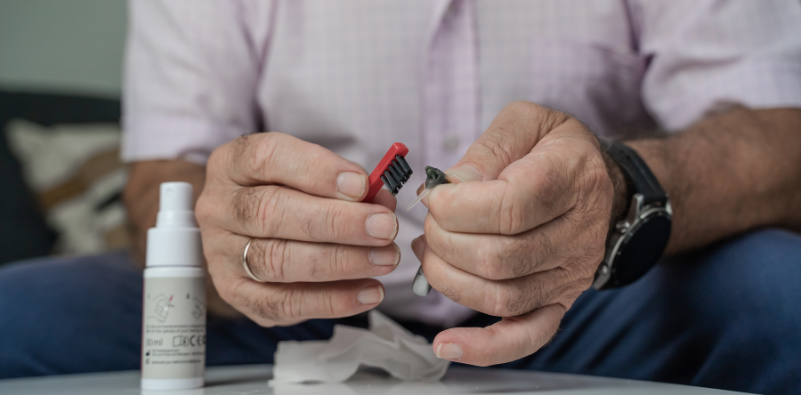 A close up image of a man cleaning his hearing aids with a brush