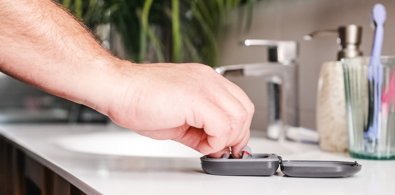 A man putting back hearing aids in a case by the bathroom sink