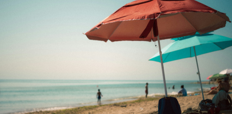 Beach scene with an orange and a blue parasol.