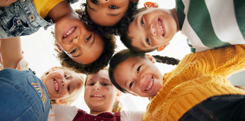 Group of smiling primary school children looking down, smiling.